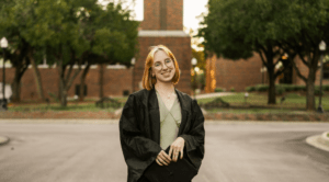 Courtney Govea posing in front of Hardin-Simmons University’s bell tower in her graduation gown.